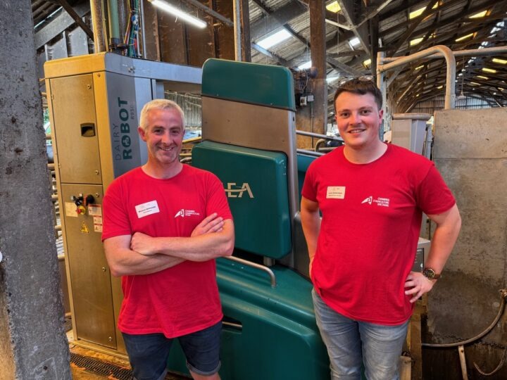 Deux hommes avec un T-shirt rouge devant un robot de traite vert.