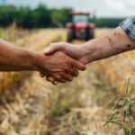 Une poignée de main dans un champ de culture avec un tracteur qui arrive dans le fond
