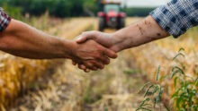 Une poignée de main dans un champ de culture avec un tracteur qui arrive dans le fond