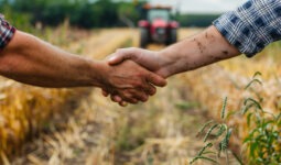 Une poignée de main dans un champ de culture avec un tracteur qui arrive dans le fond