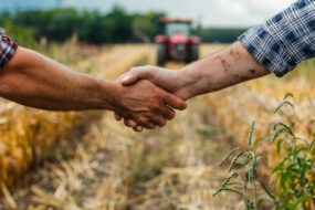 Une poignée de main dans un champ de culture avec un tracteur qui arrive dans le fond
