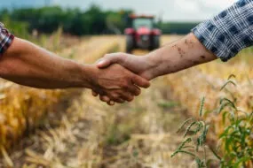 Une poignée de main dans un champ de culture avec un tracteur qui arrive dans le fond