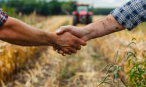 Une poignée de main dans un champ de culture avec un tracteur qui arrive dans le fond