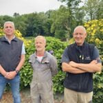 trois personnes debout devant un massif de fleurs