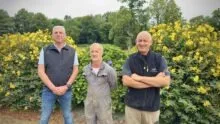 trois personnes debout devant un massif de fleurs