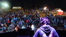 Un DJ de dos sur une scène avec une foule devant en train de danser dans une fête de l'agriculture