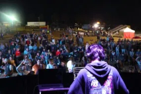 Un DJ de dos sur une scène avec une foule devant en train de danser dans une fête de l'agriculture