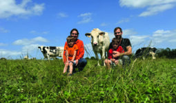 Un couple d'élevurs et leurs deux fils dans une prairie avec des vaches de race Holstein.