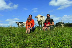 Un couple d'élevurs et leurs deux fils dans une prairie avec des vaches de race Holstein.