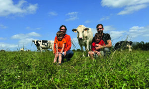 Un couple d'élevurs et leurs deux fils dans une prairie avec des vaches de race Holstein.