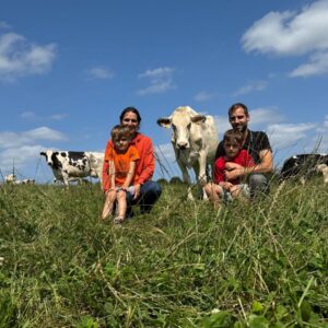 Un couple et 2 enfants assis dans un champ avec des vaches autour
