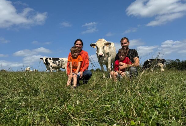 Un couple et 2 enfants assis dans un champ avec des vaches autour