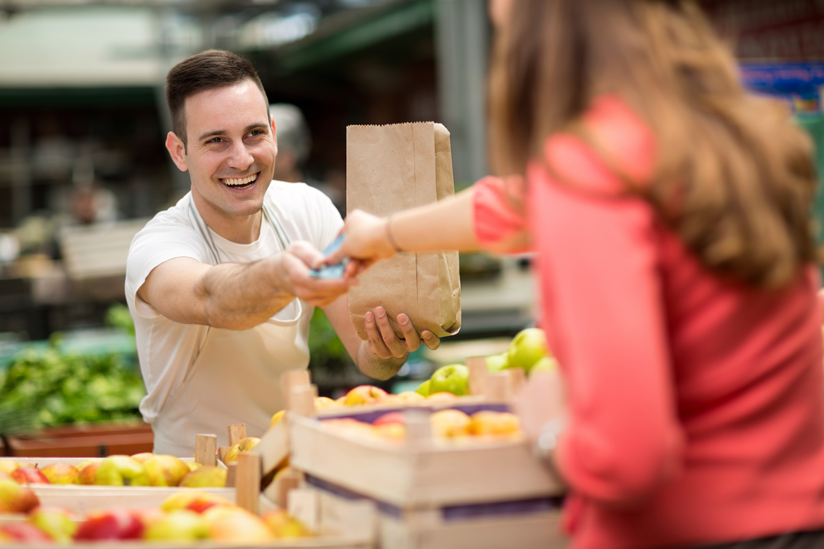 Un commerçant sur un marché de fruits et légumes qui prend la monnaie d'une cliente - Illustration Travailler son réseau professionnel localement