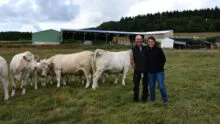 des éleveurs avec des vaches charolaises devant des bâtiments