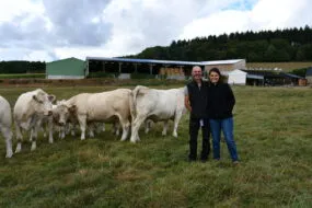 des éleveurs avec des vaches charolaises devant des bâtiments