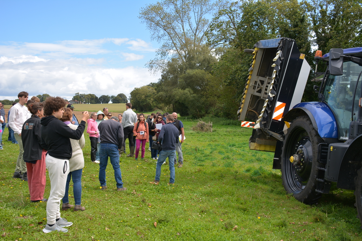 Groupe de personnes dans un champ devant un tracteur - Illustration La Cuma s’attaque au rumex