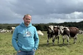 Un éleveur devant des vaches de race Normande dans une prairie.