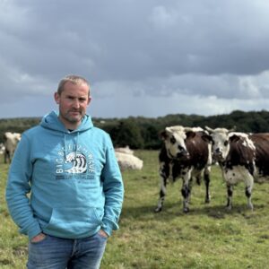 Un éleveur devant des vaches de race Normande dans une prairie.
