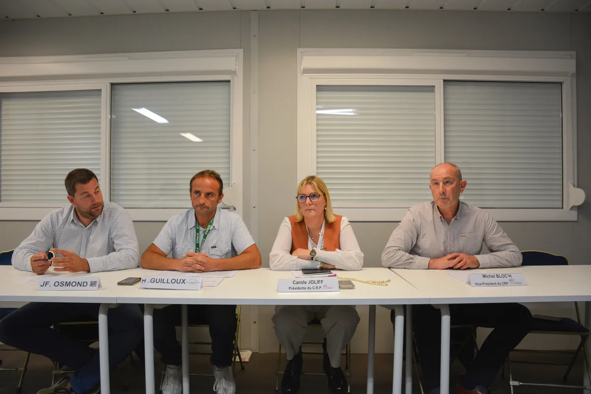 Quatre personnes assises à une table face à une assemblée - Illustration Le prix du porc décroche