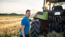Un homme à l'arrière d'un tracteur avec une main posée sur la roue dans un champ de céréales