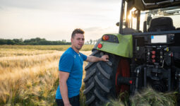 Un homme à l'arrière d'un tracteur avec une main posée sur la roue dans un champ de céréales