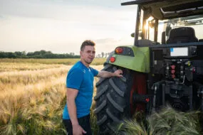 Un homme à l'arrière d'un tracteur avec une main posée sur la roue dans un champ de céréales
