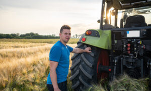 Un homme à l'arrière d'un tracteur avec une main posée sur la roue dans un champ de céréales