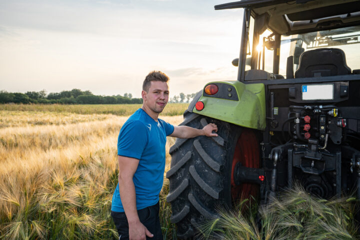 Un homme à l'arrière d'un tracteur avec une main posée sur la roue dans un champ de céréales