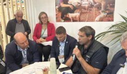Un groupe de personne autour d'une table en train d'écouter un homme qui parle avec un micro à la main