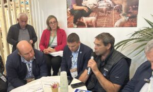 Un groupe de personne autour d'une table en train d'écouter un homme qui parle avec un micro à la main