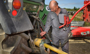 Un homme à l'arrière d'un tracteur en train d'attacher la chainette du cardan d'un outil au tracteur