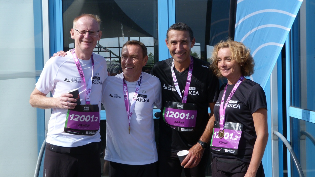 Trois hommes et une femme souriants avec des médailles autour du coup à l'arrivée d'une course