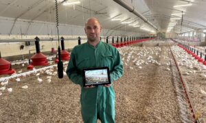 Un agriculteur dans un poulailler à côté d'un micro suspendu avec une tablette dans les mains