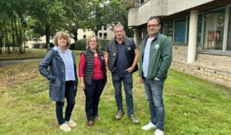 Deux hommes et deux femmes posent devant un bâtiment sur une pelouse