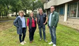 Deux hommes et deux femmes posent devant un bâtiment sur une pelouse