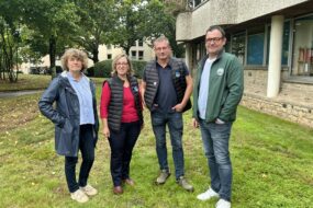 Deux hommes et deux femmes posent devant un bâtiment sur une pelouse