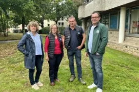 Deux hommes et deux femmes posent devant un bâtiment sur une pelouse