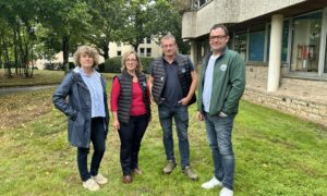 Deux hommes et deux femmes posent devant un bâtiment sur une pelouse