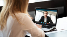 une femme de dos devant un écran d'ordinateur portable en visioconférence avec un homme