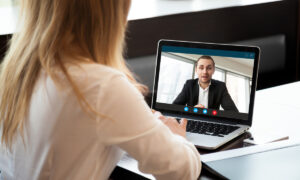 une femme de dos devant un écran d'ordinateur portable en visioconférence avec un homme