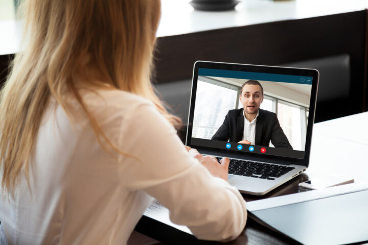 une femme de dos devant un écran d'ordinateur portable en visioconférence avec un homme