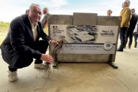 Une personne accroupie avec un brin de lin devant une affiche du pays de Landivisiau