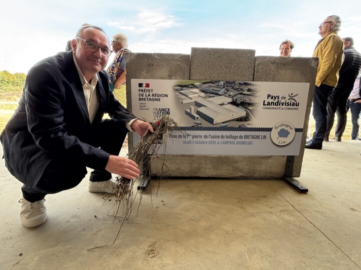 Une personne accroupie avec un brin de lin devant une affiche du pays de Landivisiau