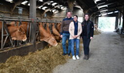 deux femmes et un homme dans une stabulation avec des vaches au cornadis