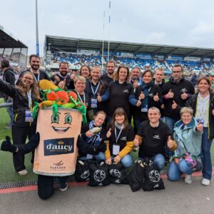 Un groupe de personne avec une mascotte d'Aucy dans un stade de rugby