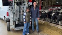 Une jeune femme et un homme devant une cage de parage à côté de vaches de race Holstein au cornadis