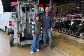 Une jeune femme et un homme devant une cage de parage à côté de vaches de race Holstein au cornadis