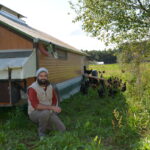 un homme accroupi à côté d'un poulailler mobile d'un élevage de volailles