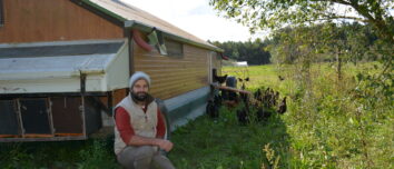 un homme accroupi à côté d'un poulailler mobile d'un élevage de volailles