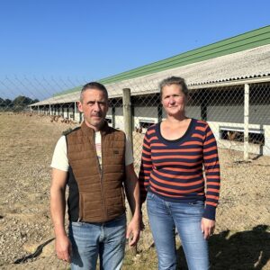 Un homme et une femme devant un bâtiment d'élevage de volailles